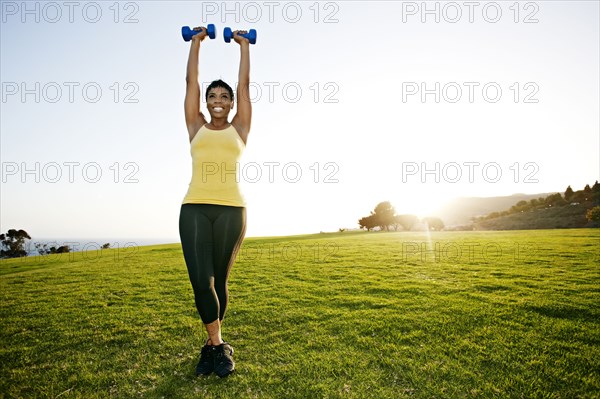 Black woman lifting weights in field