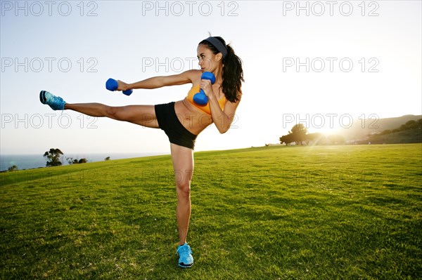 Hispanic woman lifting weights in field