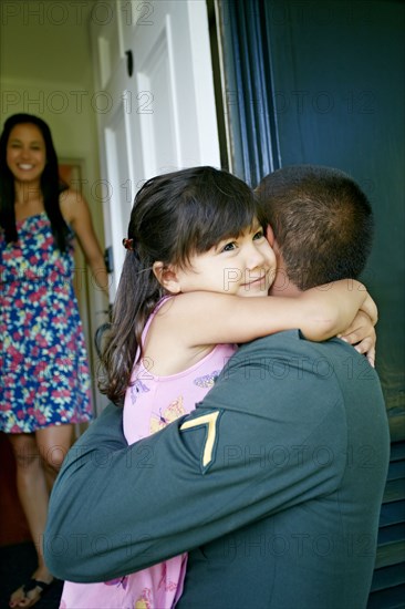 Girl hugging soldier father at door