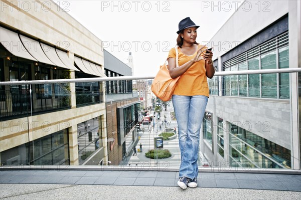 Black woman using cell phone on sky bridge at shopping mall