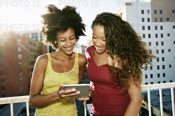 Mixed race women using digital tablet on urban rooftop