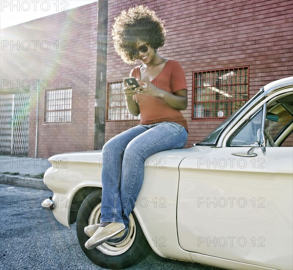 Mixed race woman sitting on vintage car