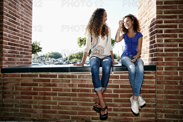 Mixed race girls sitting on brick ledge