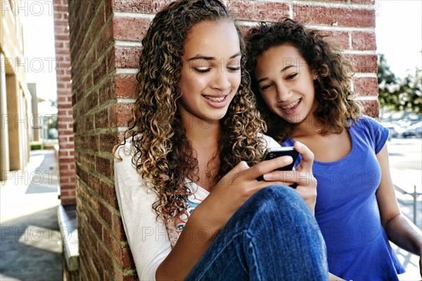 Mixed race girls using cell phone outdoors