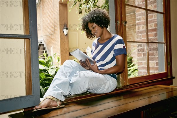 Mixed race woman using digital tablet in windowsill