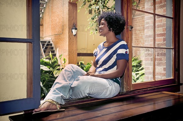 Mixed race woman sitting in windowsill