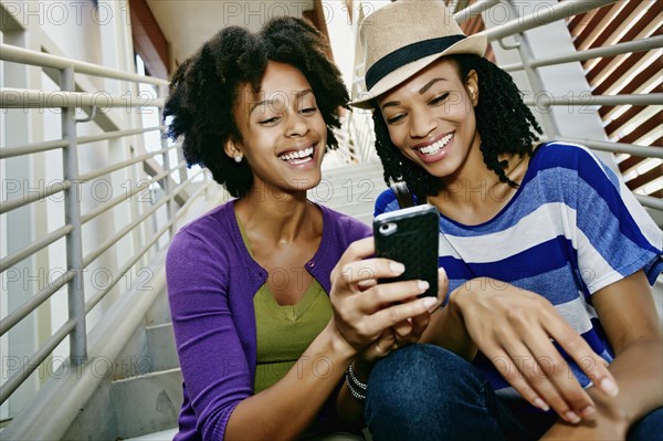 Women using cell phone together on steps