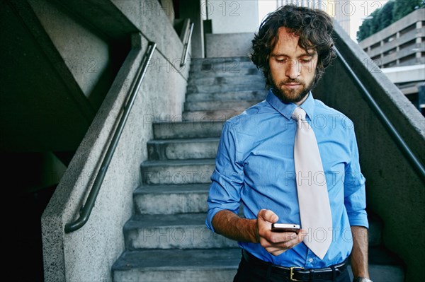 Caucasian businessman using cell phone on urban stairs