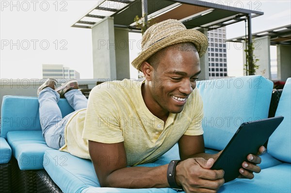 Black man using digital tablet on sofa on urban rooftop