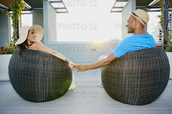 Couple holding hands in wicker chairs on balcony