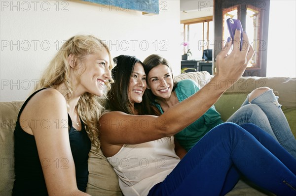 Women taking self-portraits together on sofa