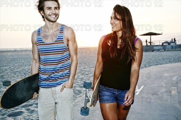 Couple carrying skateboards on beach