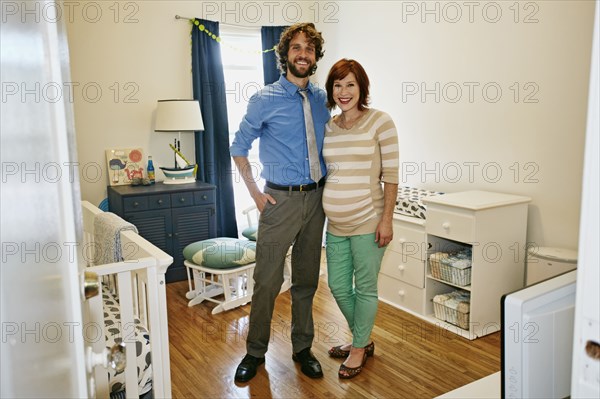 Pregnant Caucasian couple smiling in nursery