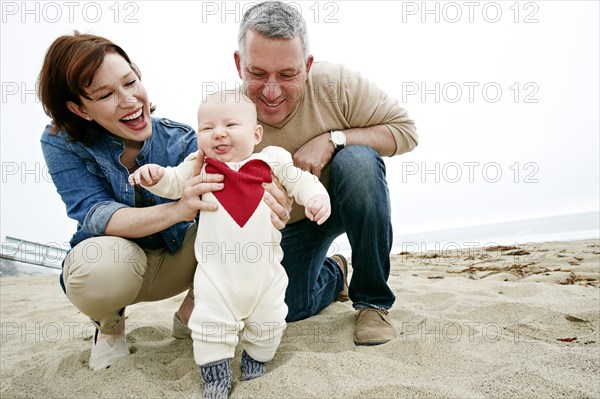 Parents helping baby walk on beach