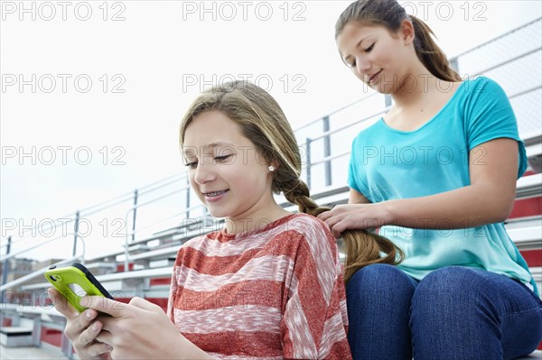 Teenage girl braiding friend's hair in bleachers