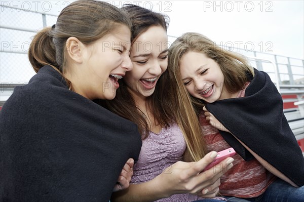 Teenage girls using cell phone in blanket