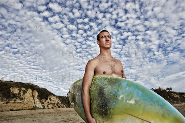 Caucasian man carrying surfboard on beach