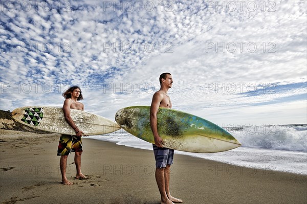 Caucasian men carrying surfboards on beach