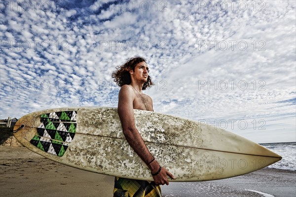 Caucasian man carrying surfboard on beach