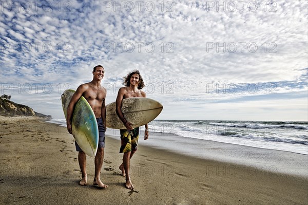 Caucasian men carrying surfboards on beach