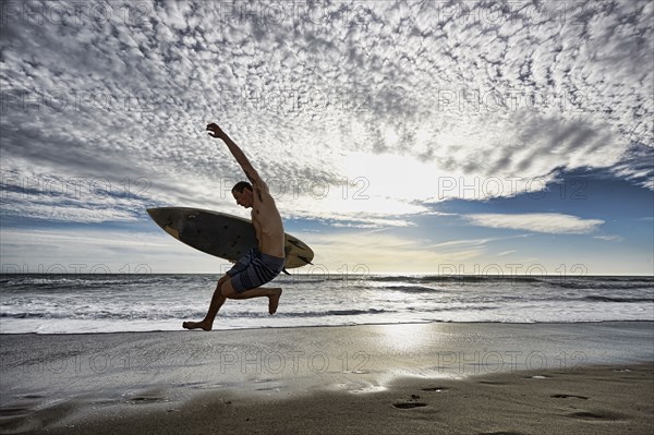 Caucasian man jumping with surfboard on beach