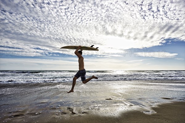 Caucasian man jumping with surfboard on beach