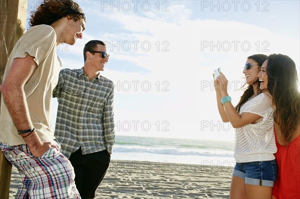 Women taking picture of boyfriends on beach