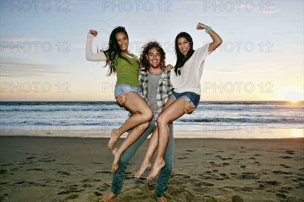 Man holding women on each arm on beach