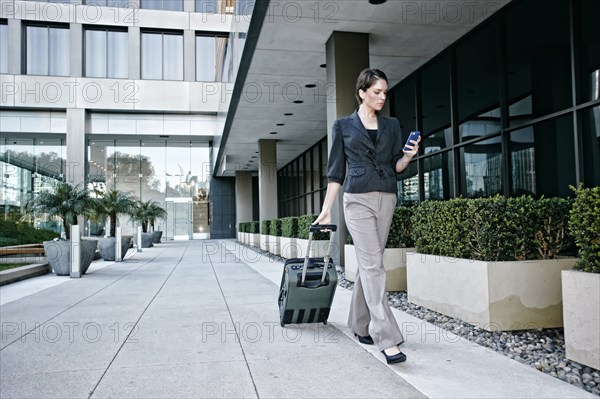 Caucasian businesswoman rolling baggage outdoors