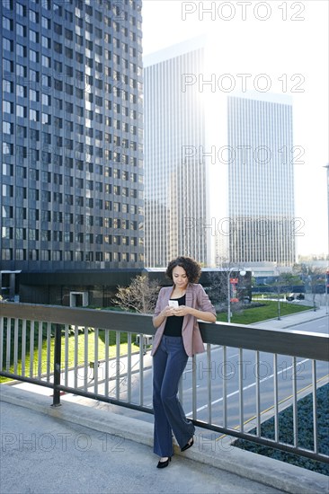 Mixed race businesswoman using cell phone on urban sky bridge