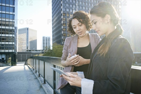 Businesswomen using tablet computer on urban sky bridge