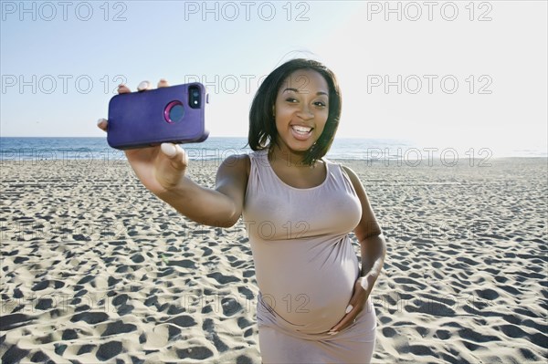 Pregnant woman taking cell phone picture on beach