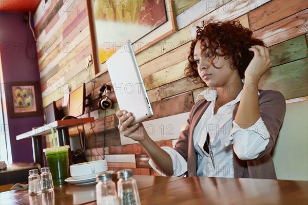 Mixed race woman using tablet computer in cafe