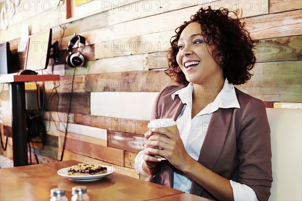 Mixed race businesswoman having coffee and pastry in cafe