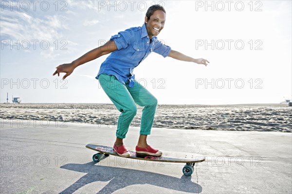 Older Black woman skateboarding by beach