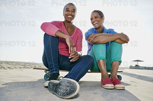 Older Black women sitting on skateboard on beach