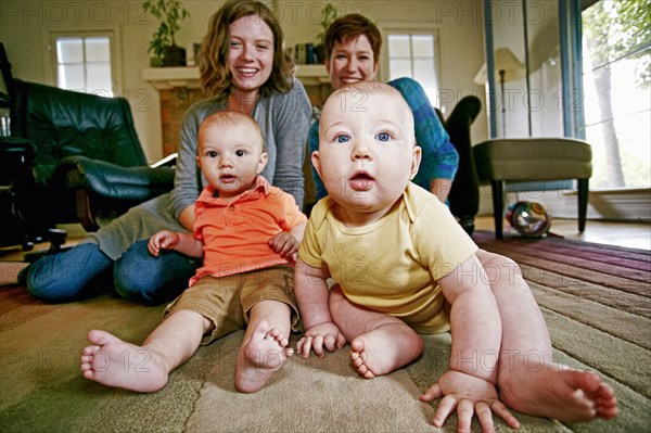 Caucasian mothers and babies sitting on living room floor