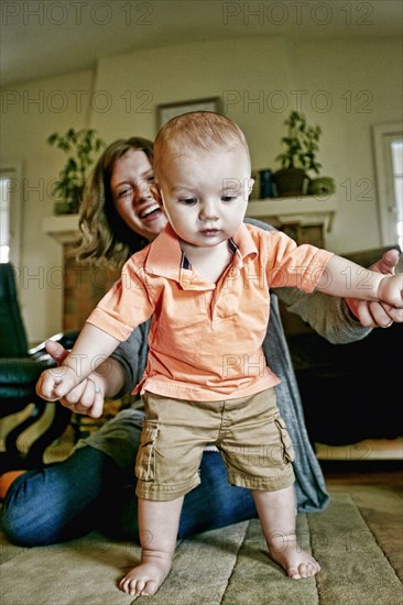 Caucasian mother helping baby walk on living room floor