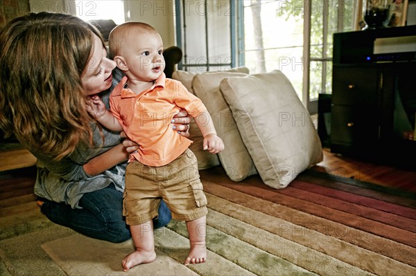 Caucasian mother helping baby walk on living room floor