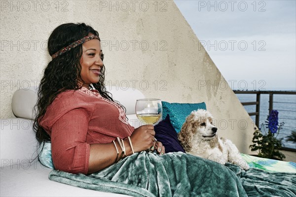 Mixed race woman drinking wine at waterfront with dog