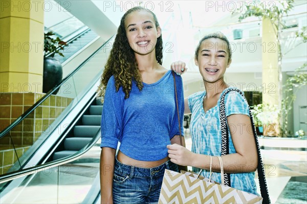 Mixed race teenage girls shopping near escalator at shopping mall