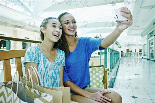 Mixed race teenage girls taking cell phone photograph at shopping mall