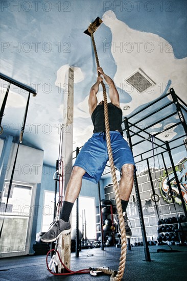 African American man climbing rope in gym