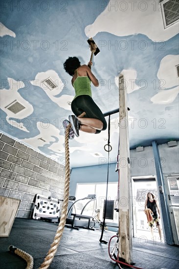 African American woman climbing rope in gym