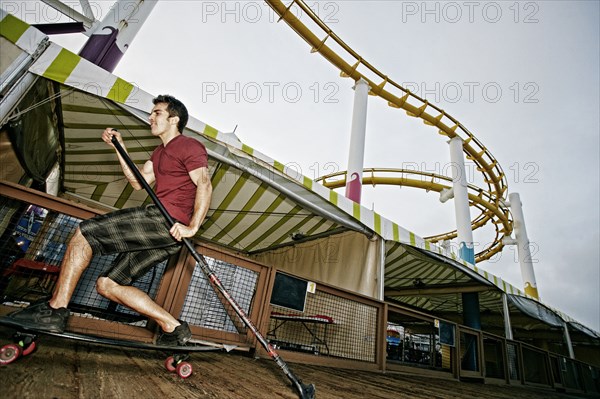 Caucasian man skateboarding with paddle pole at amusement park