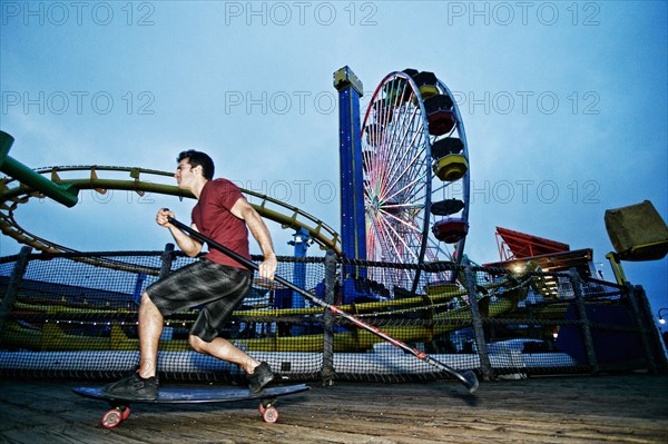 Caucasian man skateboarding with paddle pole at amusement park