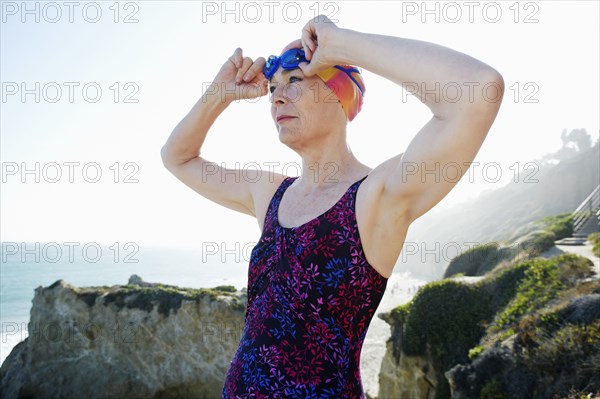 Older Caucasian woman putting on goggles on beach