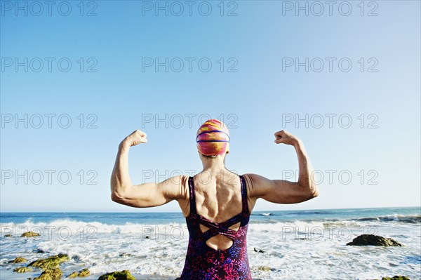 Older Caucasian woman flexing her muscles on beach