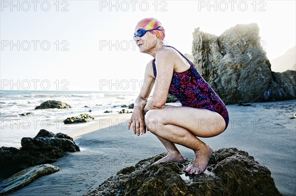 Older Caucasian woman crouching on rock on beach