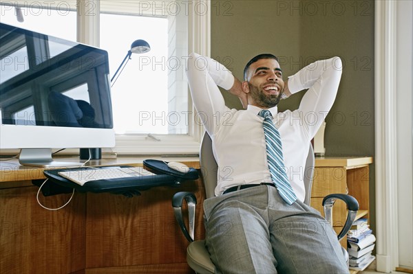 Middle Eastern businessman relaxing in chair at desk in office